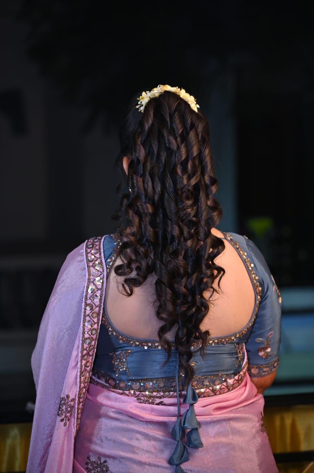 Curled bridal hairstyle with floral accessory styled at Prayosha Salon